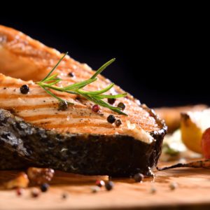Grilled salmon fish and various vegetables on wooden table on black background