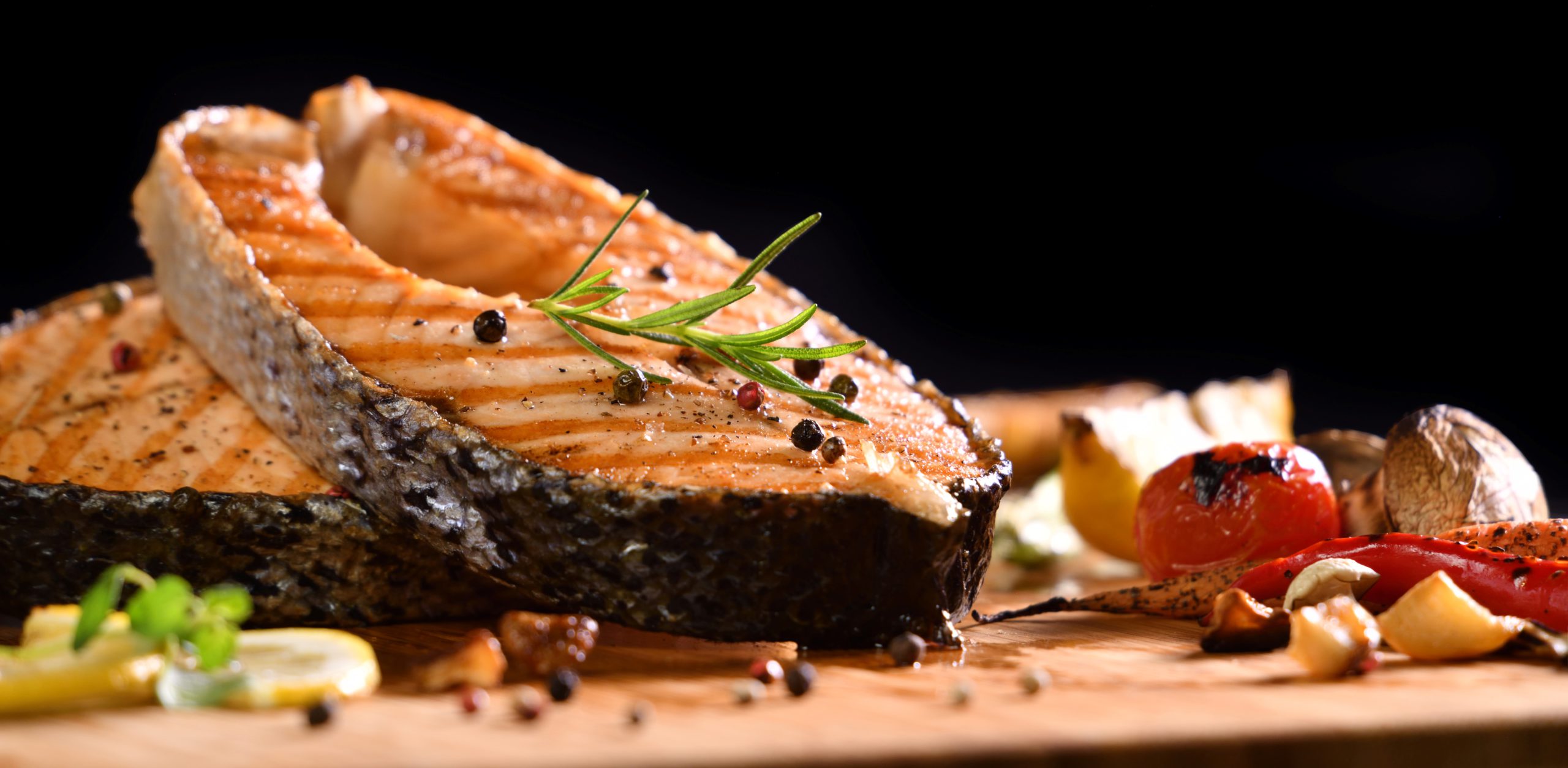 Grilled salmon fish and various vegetables on wooden table on black background